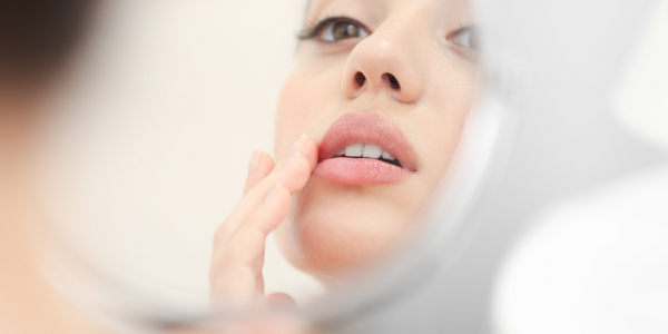 Young woman with cold sore looking in circular mirror at home.