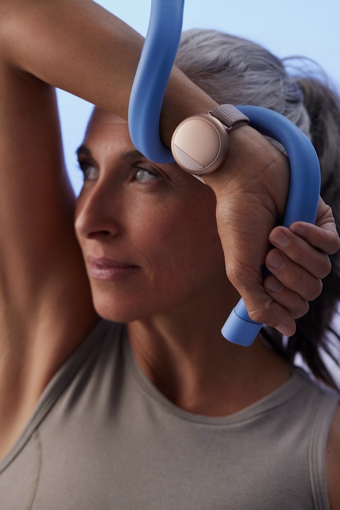 Woman stretching with a blue exercise band behind her head wearing the Embr Wave.