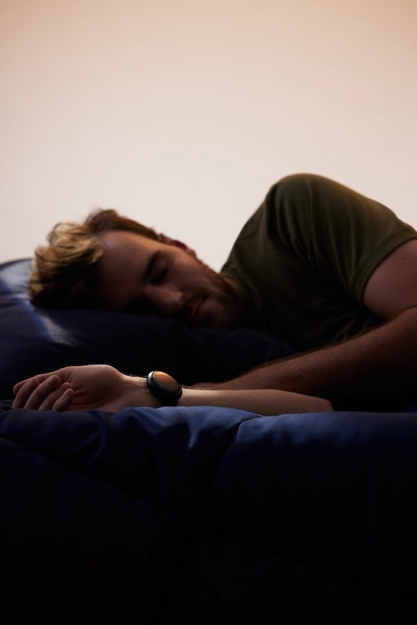 Man sleeping comfortably with an Embr Wave wearable device on his wrist.