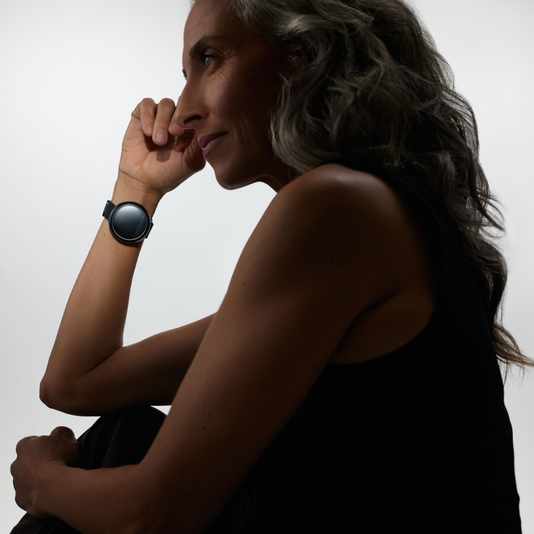 Side profile of a contemplative woman with a smartwatch, against a light background.