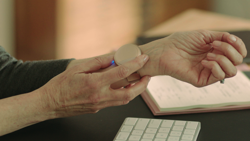 Woman adjusting the rose gold Embr Wave 2 on her left wrist at her desk.