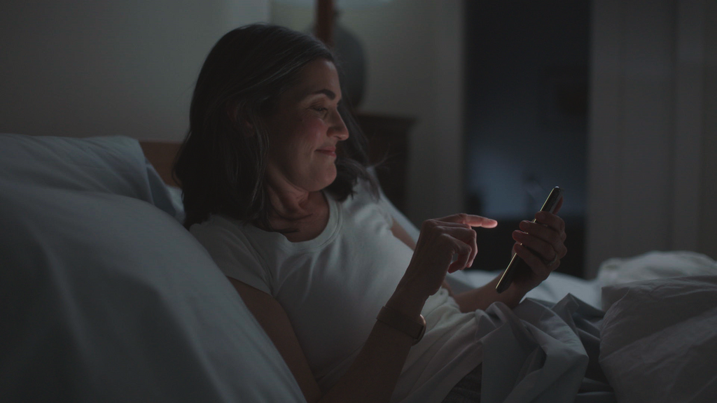 Woman using her smartphone in bed while wearing the Embr Wave bracelet.