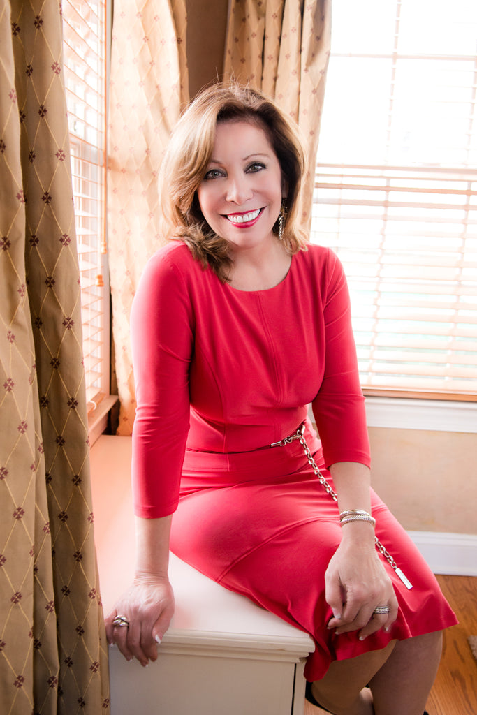 Smiling woman in red dress sitting by sunny window.