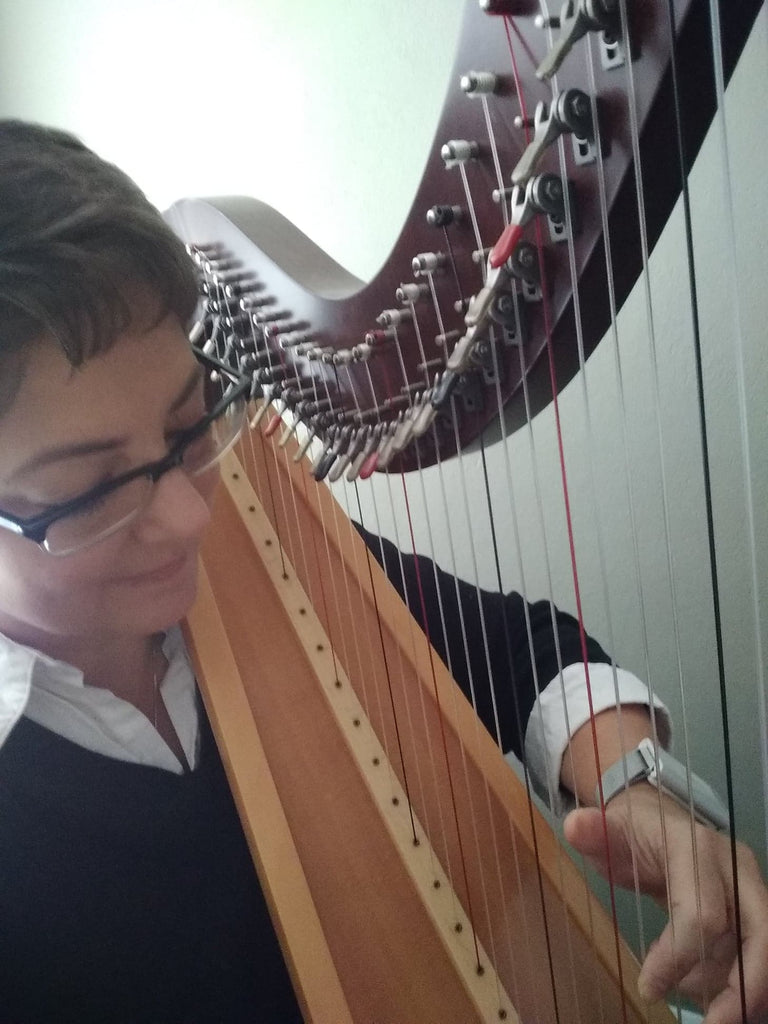 Smiling woman with glasses playing the harp and wearing the silver Embr Wave 1 bracelet.