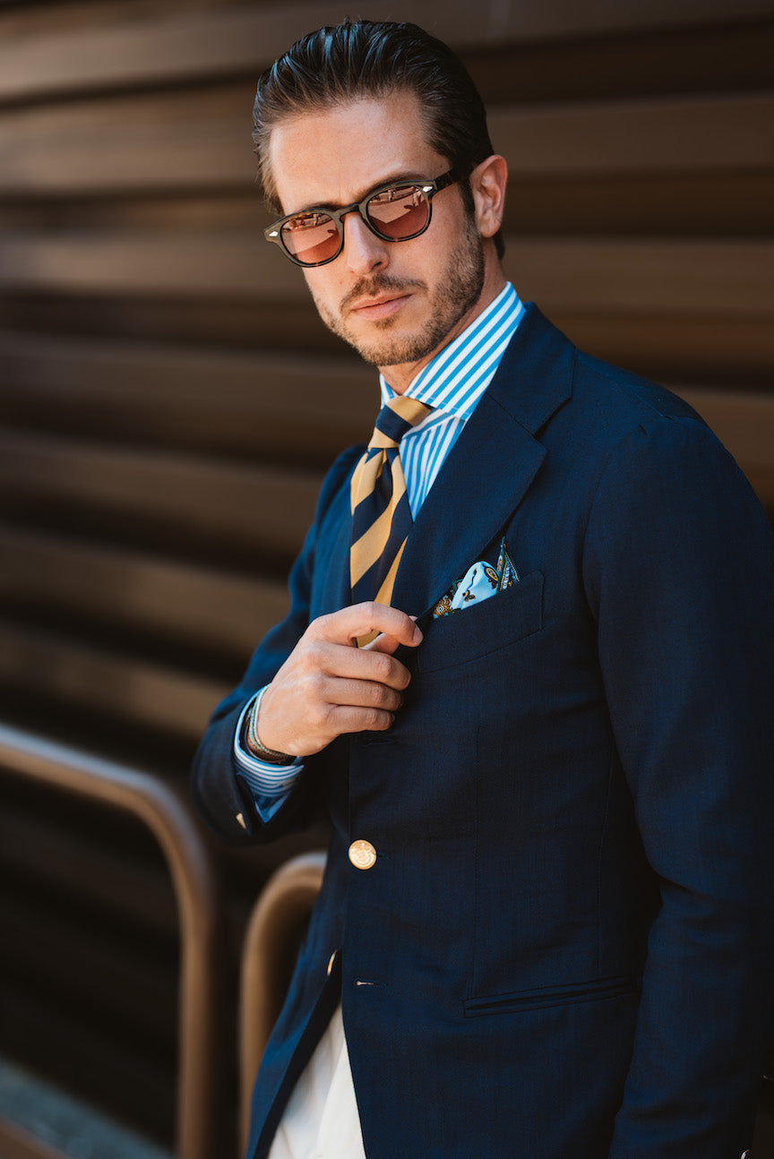 Man wearing sunglasses in navy suit jacket and tie with pocket squre