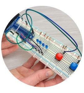 Against background of grey wood table, two hands hold up a breadboard circuit including GPIO header, jumper wires, blue LEDs, resistors, and pushbutton switches