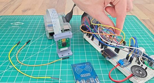 Breadboard circuit with assorted electronic components sitting on green engineering mat; hand is adjusting jumper wire on circuit