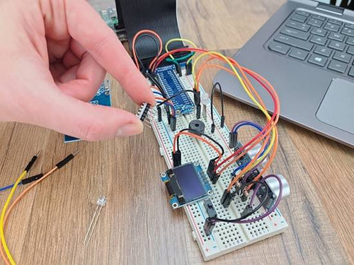 Hand placing temperature sensor in breadboard circuit on wood table next to laptop