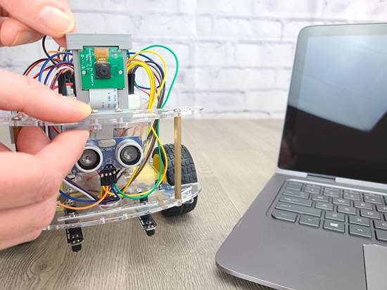 Hands adjusting components on robot sitting on desk next to laptop