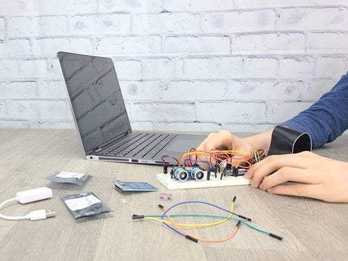 Hands working on breadboard circuit with electronic components and laptop computer on wood table