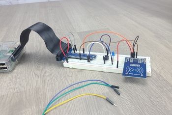 Breadboard circuit on table with RFID reader added to circuit; jumper wires on table beside circuit