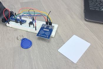 RFID breadboard circuit with all electronic components attached; RFID card, RFID tag, and laptop sitting on table next to circuit