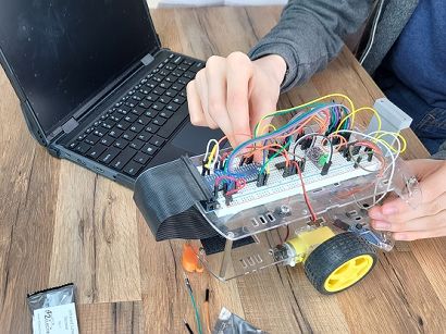 Hands working on robot with breadboard circuit. Sitting on table next to laptop.