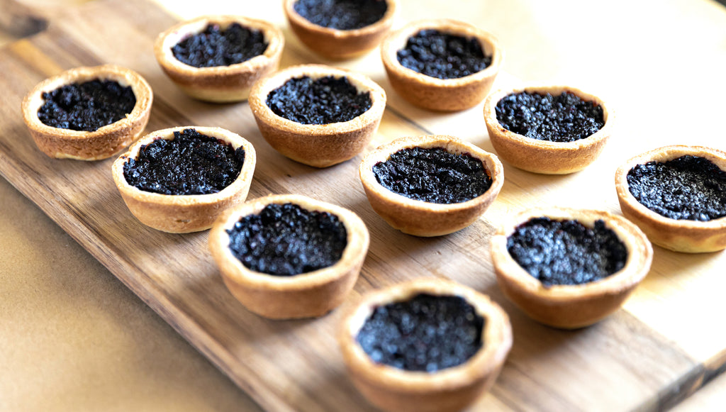 Rows of Saskatoon berry tarts on a wooden serving board. Photo by Noella Steinhauer.