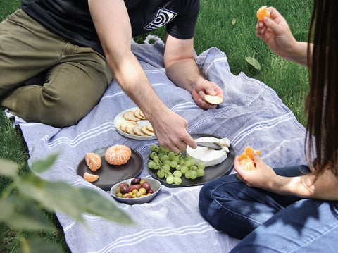 a man on a blue picnic blanket eating off a black plate with grapes and cheese