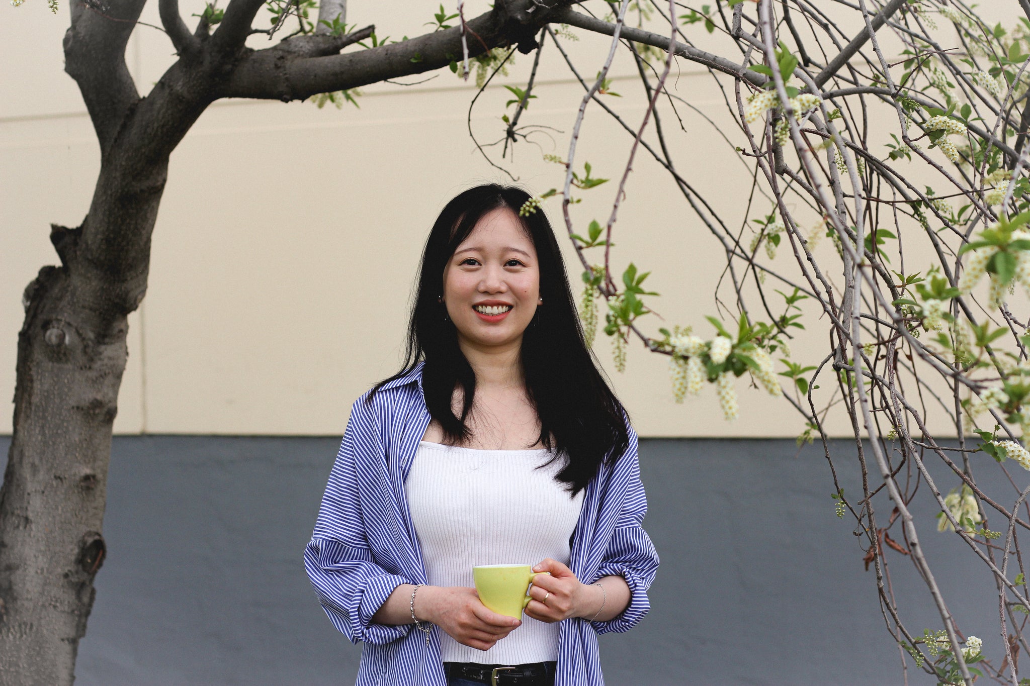 Jenny Tan holding a cup of coffee underneath a tree