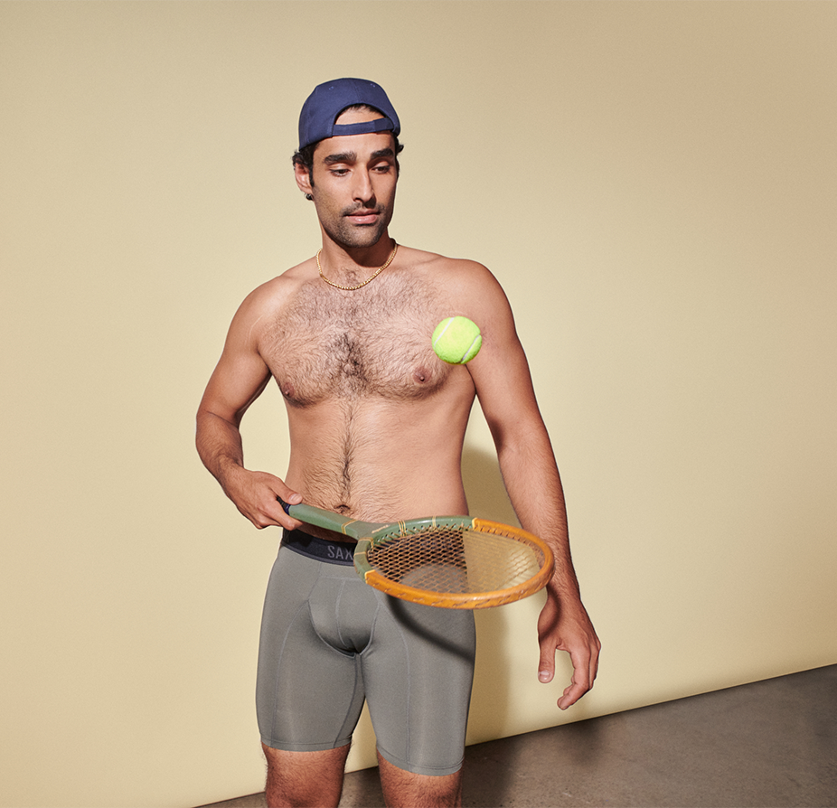 Man in grey boxer briefs and hat holding tennis racket