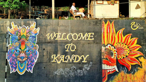 'Welcome To Kandy' Painted On A Wall Sign Outside The City Whilst A Local Man Is Enjoying An Afternoon Sit In The Sun On Top Of The Wall | Kandy | Sri Lanka | Australian Cricket Tours