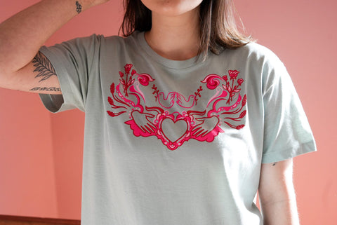 White woman wears sage green tee shirt with pink artwork on