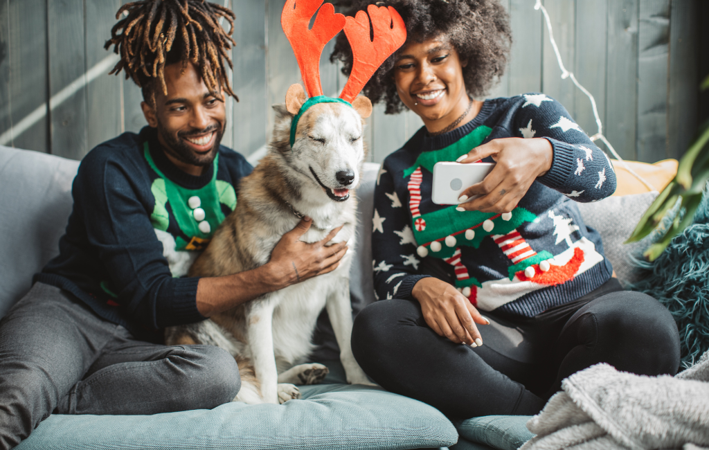 young couple celebrating Christmas with husky shepherd mutt on couch taking selfie