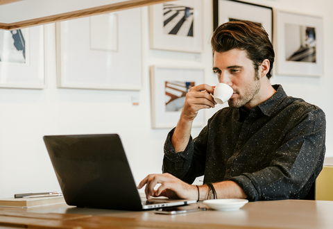man sipping coffee while working on computer