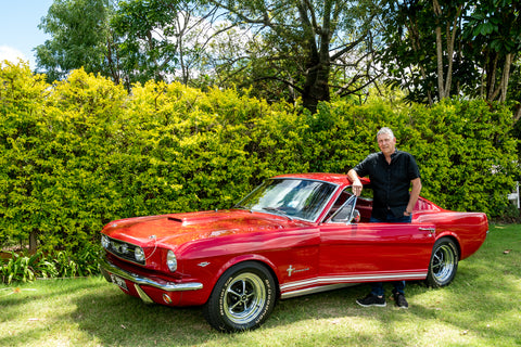 Rodney parado junto a su Mustang 66 rojo