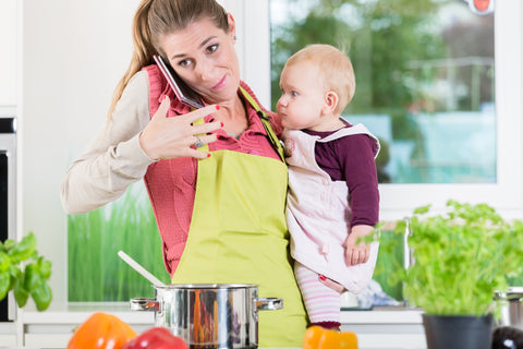 A stressed out mom in the kitchen holding a baby and trying to talk on the phone