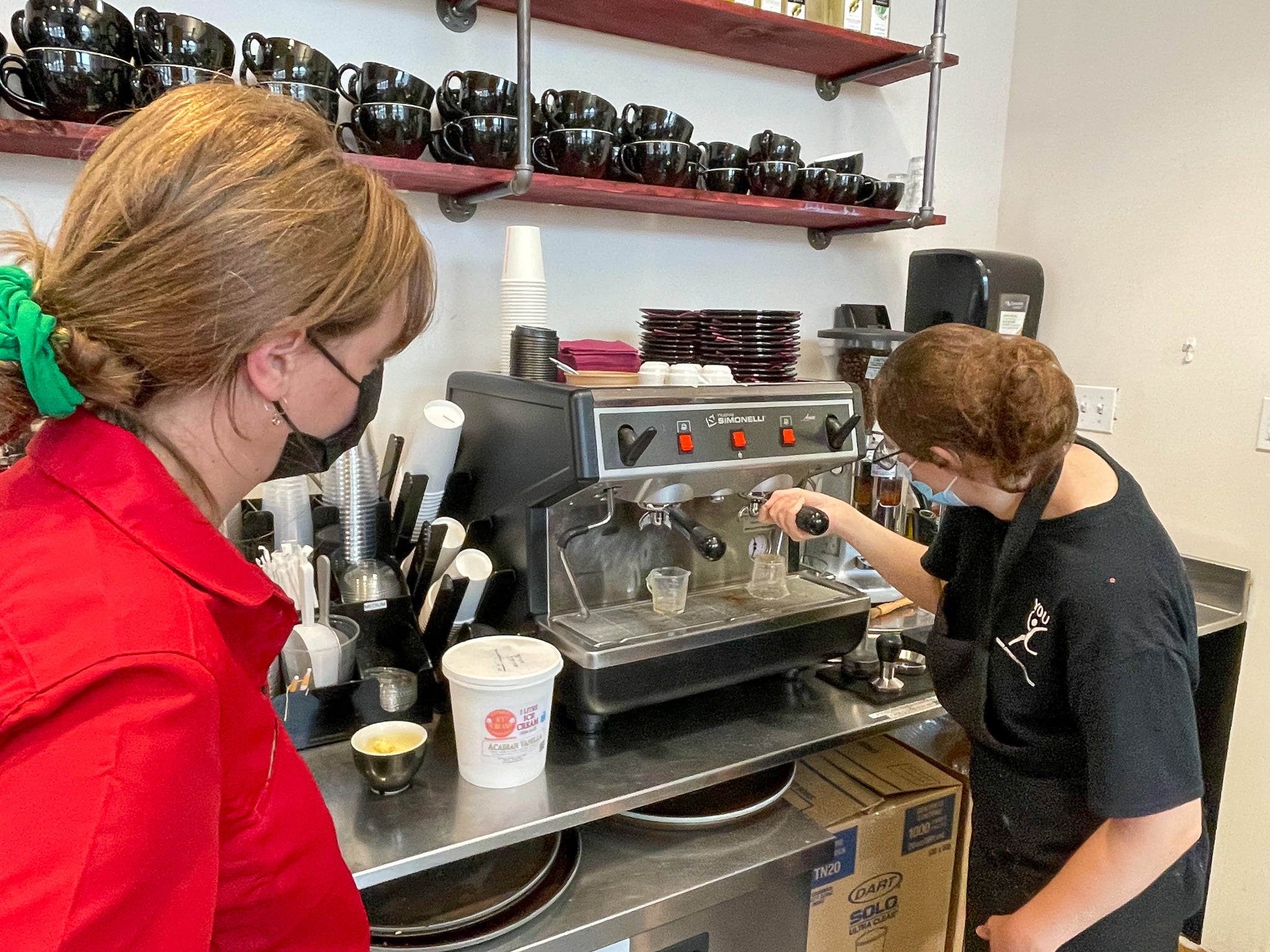 A youth mentor coaching a youth trainee on the espresso machine.