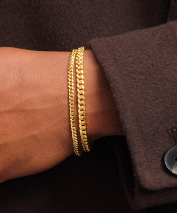 Closeup of wrist with two gold cuban link bracelets.