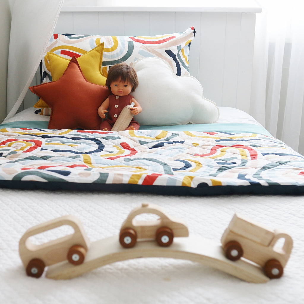 A Colourful Kids' Room with bright cushions on bed and babydoll with wooden toy bottle