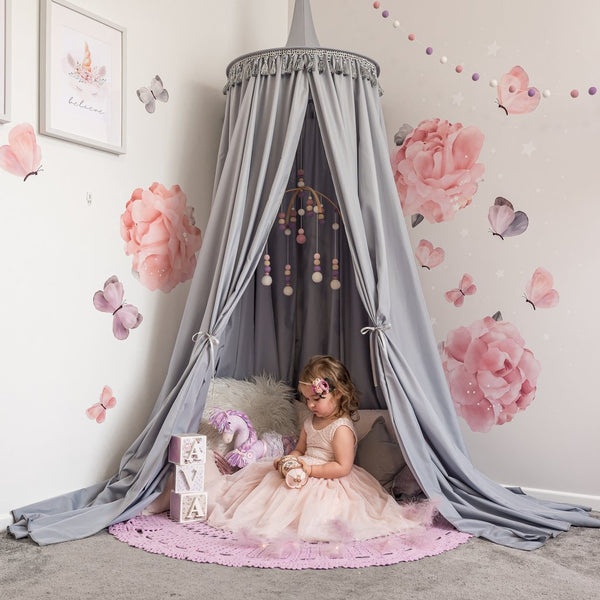 Grey canopy hanging from the ceiling in girls bedroom as reading nook with young girls sitting under canopy