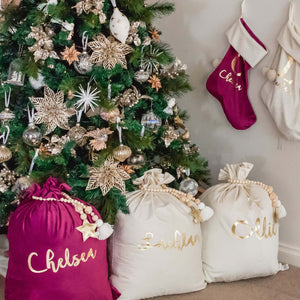 Purple and white personalised santa sacks and stockings sitting under a green christmas tree
