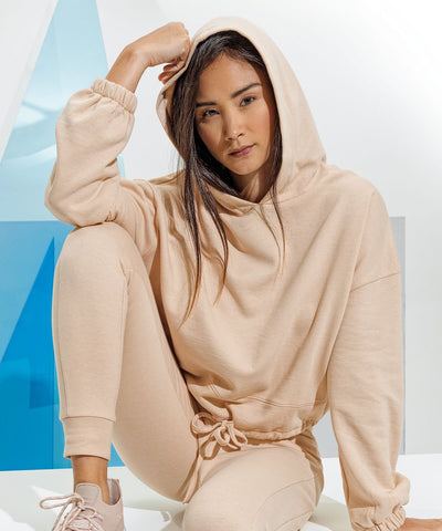  A lady sitting on white blocks with her arm resting on one raised knee. She is wearing an oversized cropped beige hoodie with matching sweatpants and sneakers.