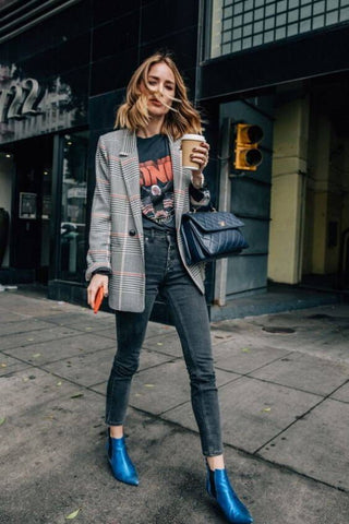 Lady wearing graphic print tee under a checked blazer with skinny jeans a pointy metallic blue ankle boots