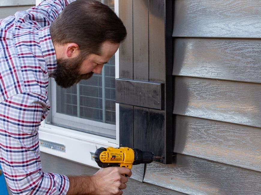 black shutters being installed on a grey house