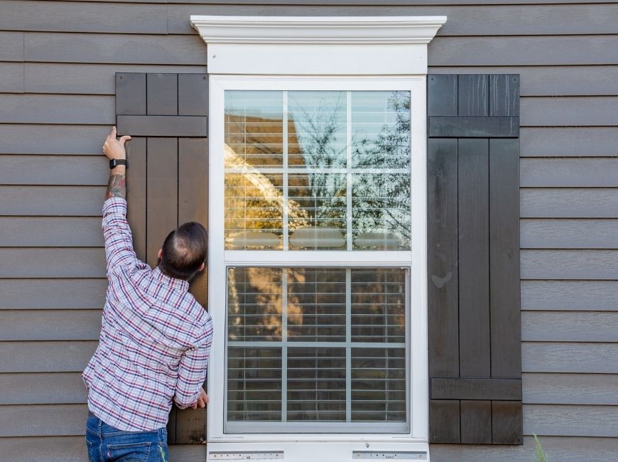 man replacing black shutters on a grey house