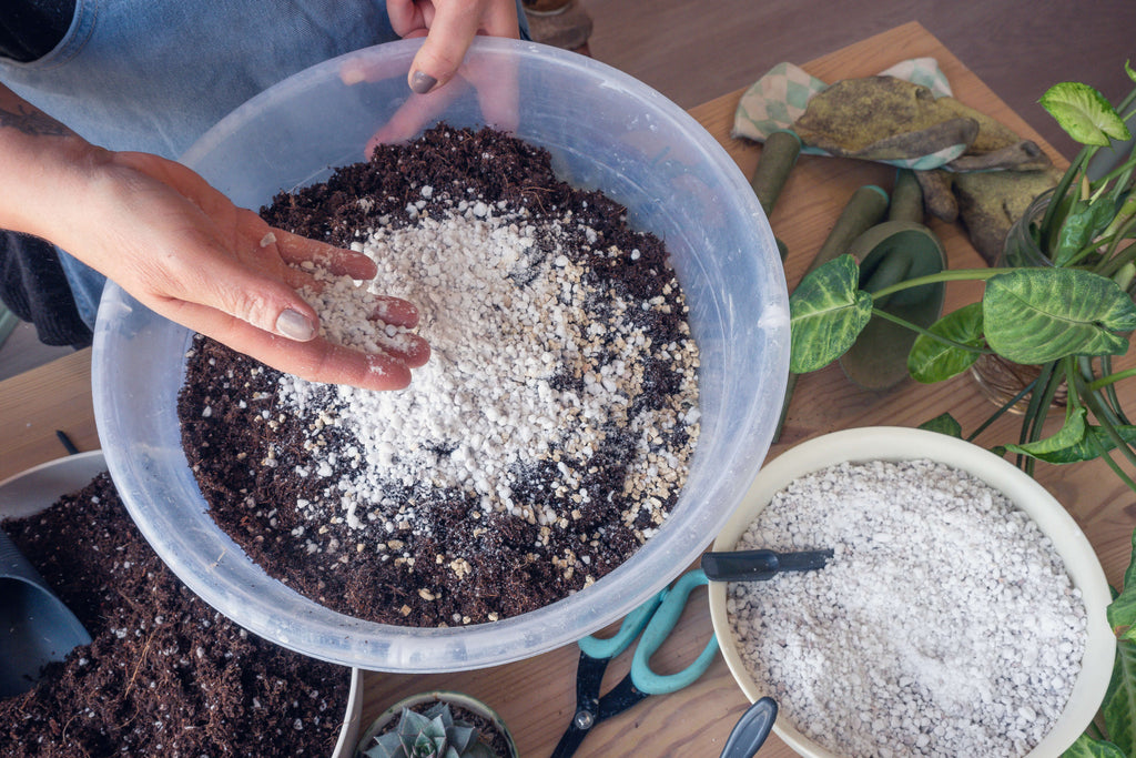 Hands holding perlite over a bucket with potting soil.