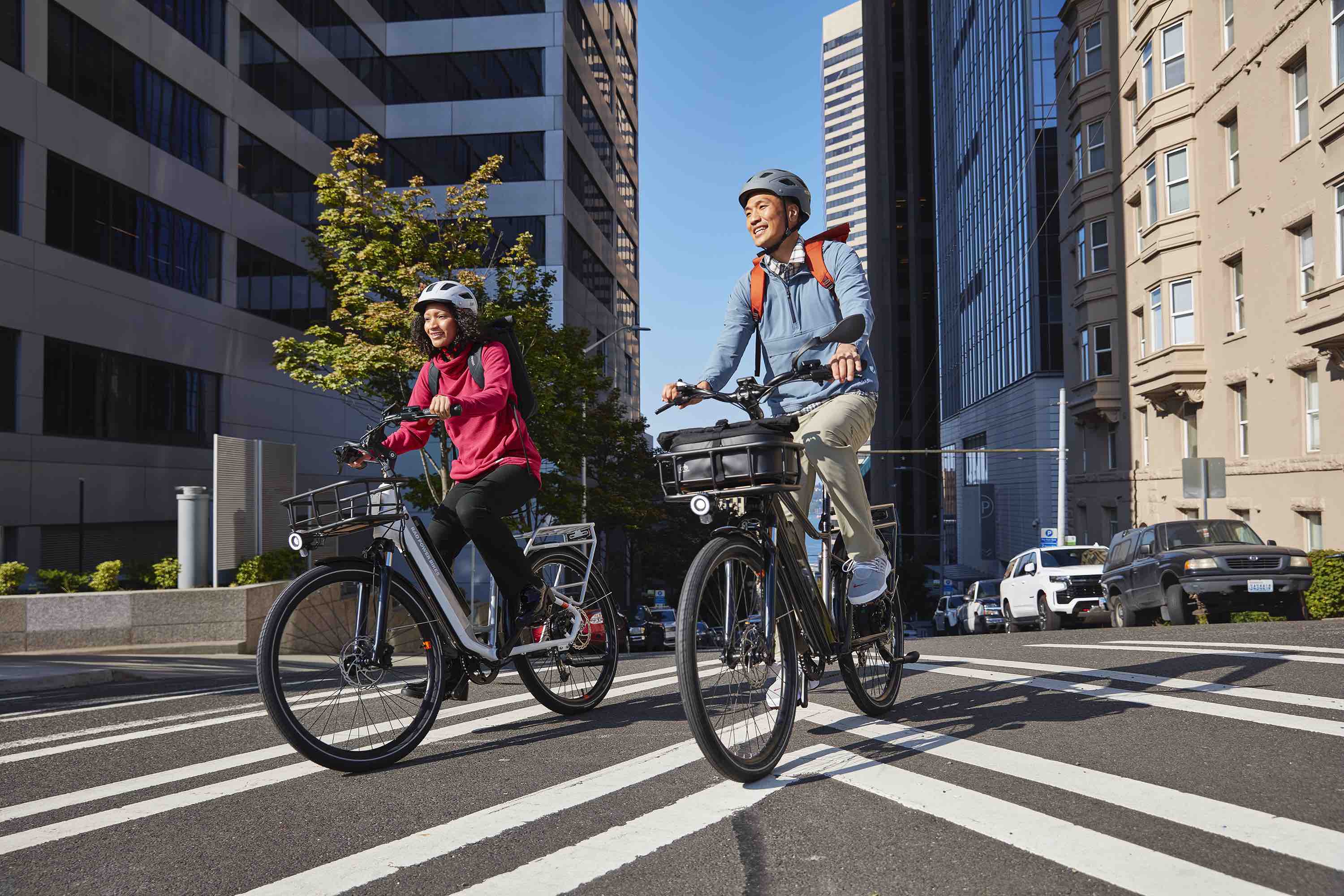 Two people ride through a city street on a RadCity 5 Plus.