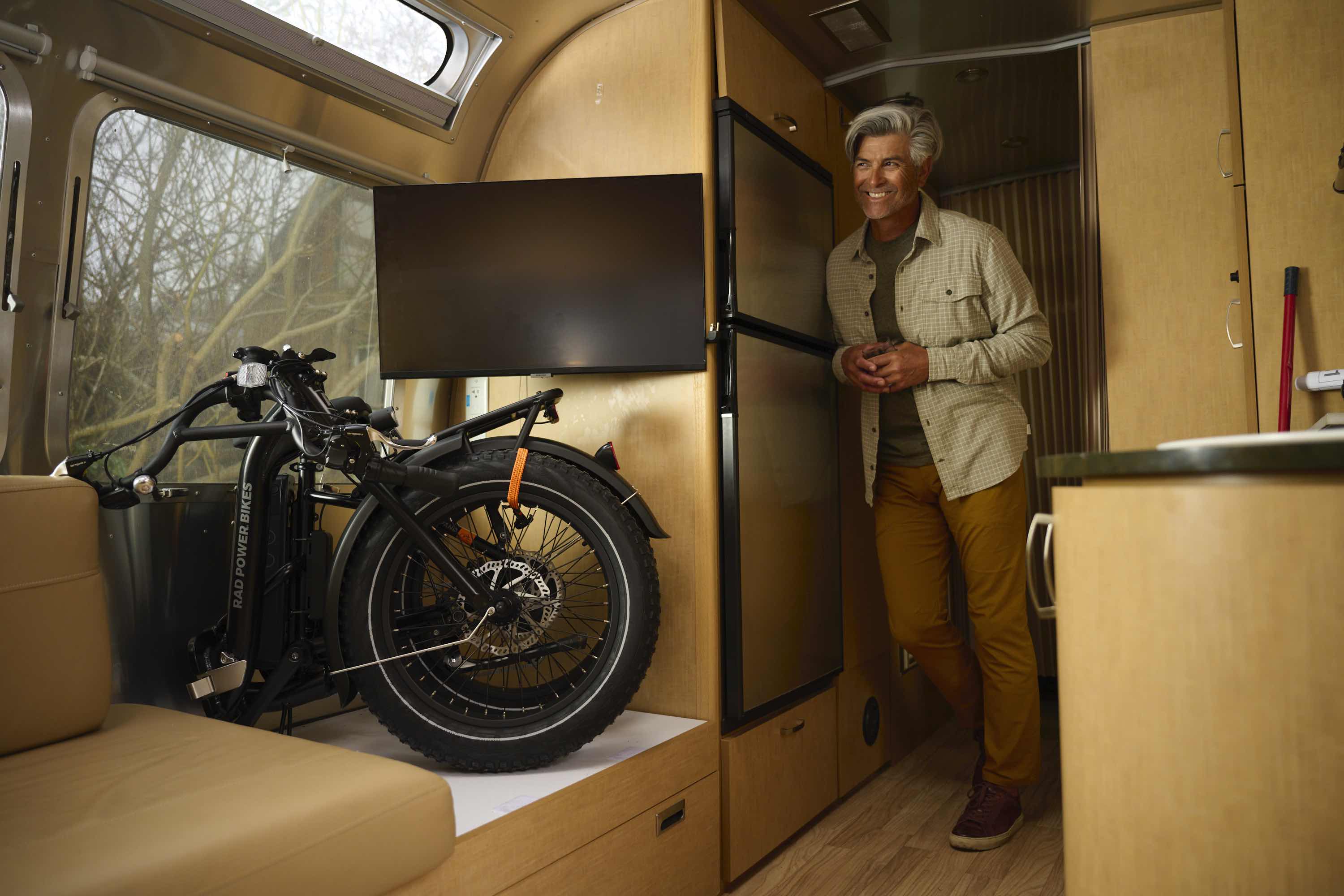 A silver haired man stands next to a folded-up RadExpand in an RV.