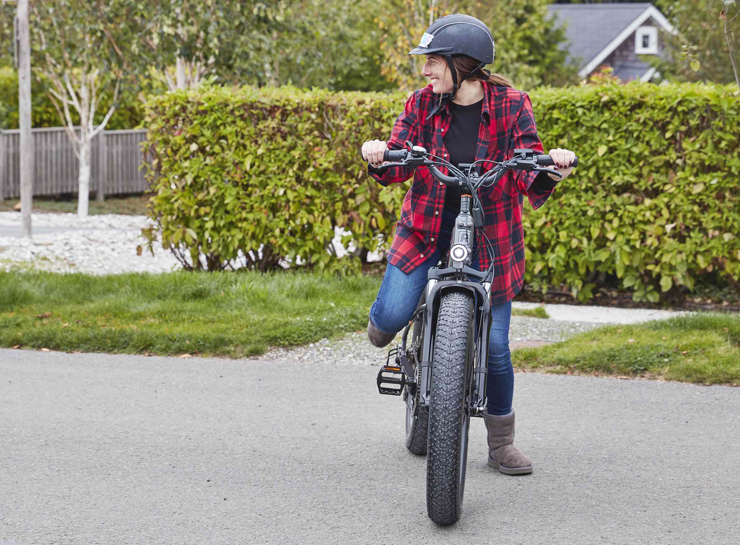 A woman in plaid rides a RadRover ebike in a suburban neighborhood while smiling.