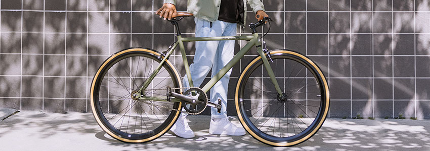 A person stands beside a bicycle featuring a distinctive green tire, showcasing a unique and vibrant design.