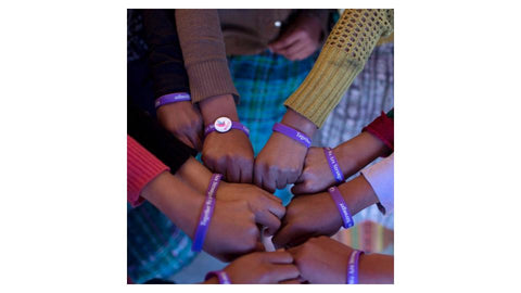A close up of the arms of a group of girls showing off their Girl Up bracelets