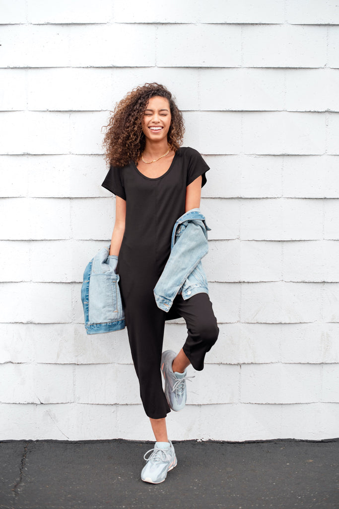 model stood against white wall wearing black smash + tess romper, denim jacket and white sneakers