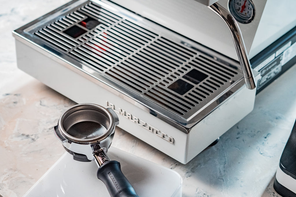 View of the Linea Mini R's wordmark, drain box, and portafilter lifestyle by Clive Coffee