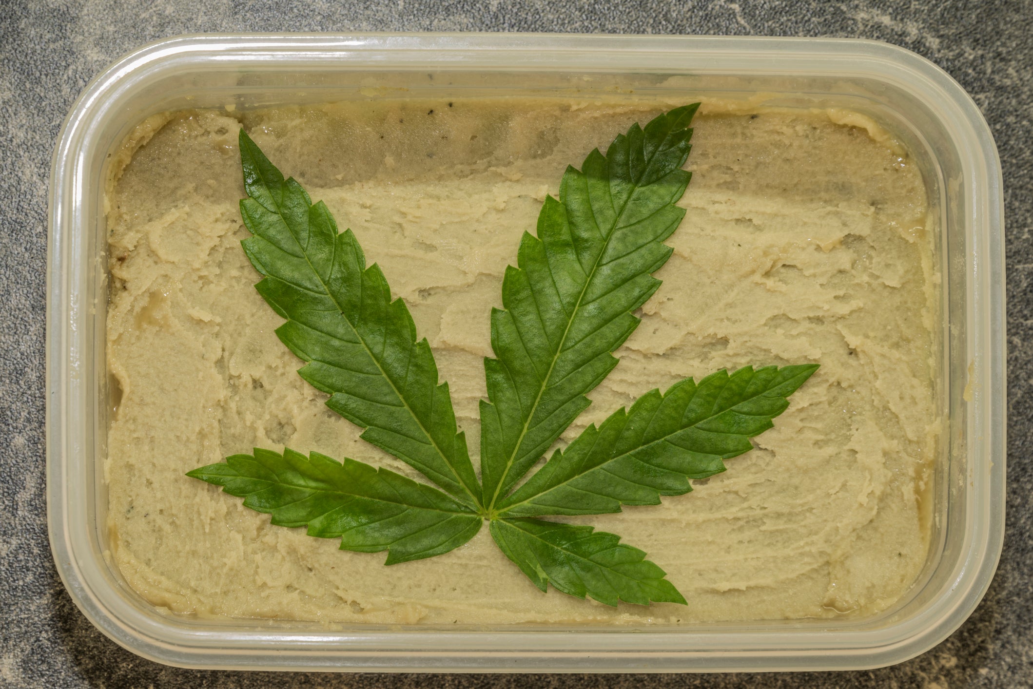 Cannabutter in a plastic container has a cannabis leaf on top of it and will be used to make cannabis edibles.