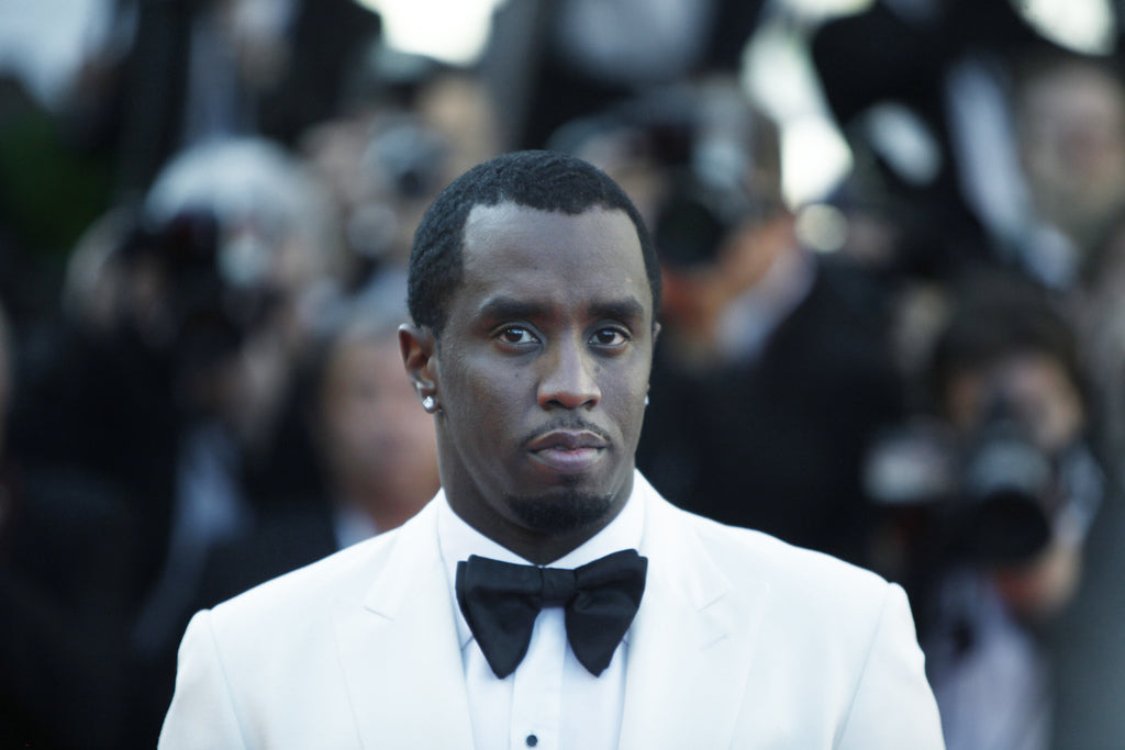 Diddy, a celebrity who loves cannabis flower, in a white tuxedo and black bow-tie, stands in front of a crowd.