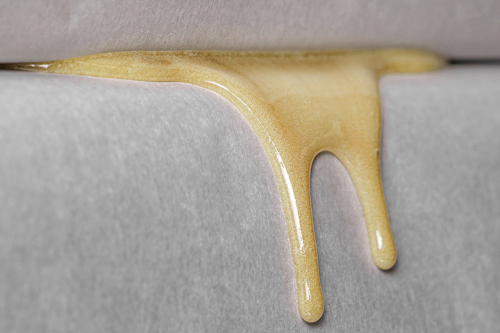 Golden streams of live rosin are dripping out of a rosin press in which pure bubble hash is heated and squeezed. 