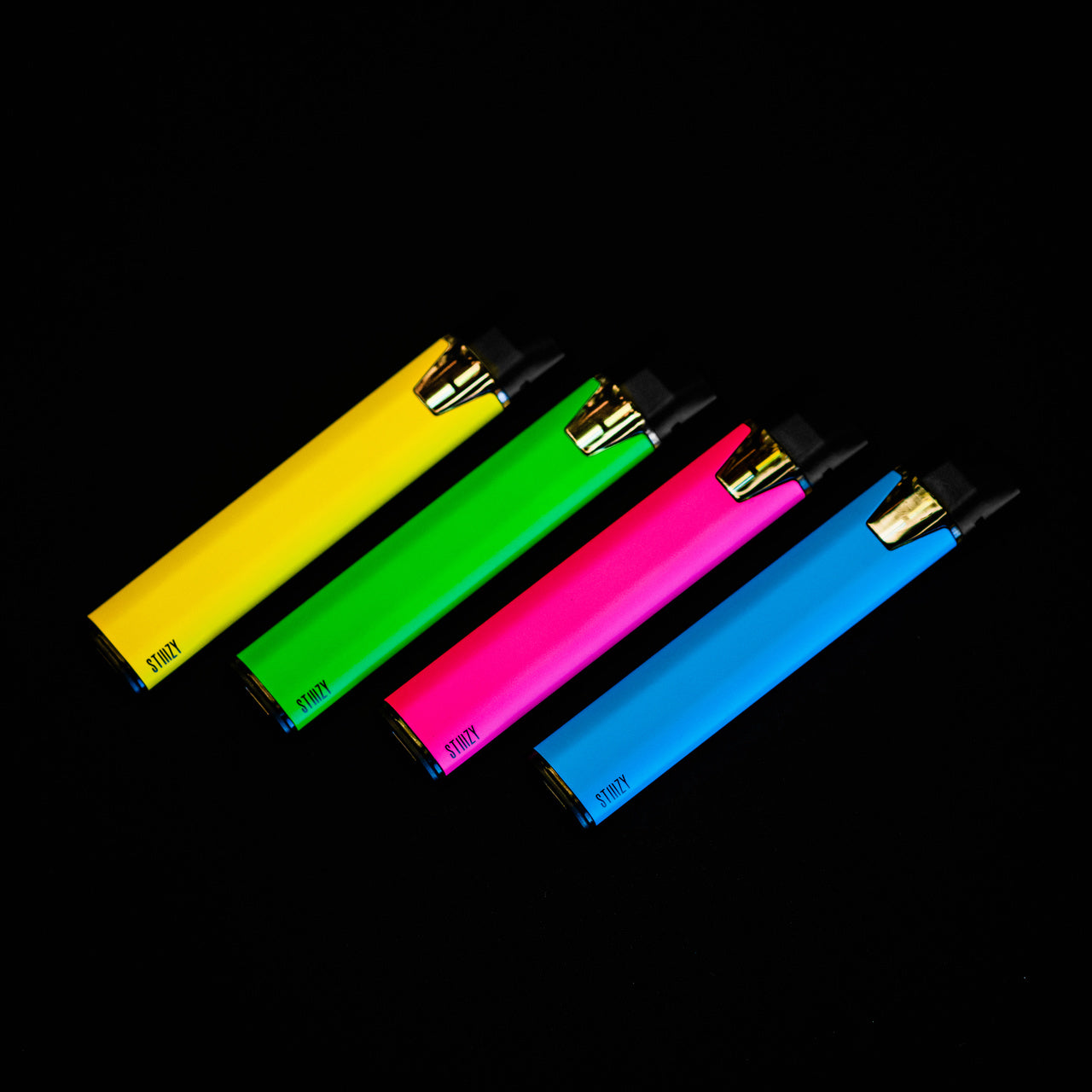 A blue, neon pink, green, and yellow weed vape pen from STIIIZY lie tilted on a black surface.