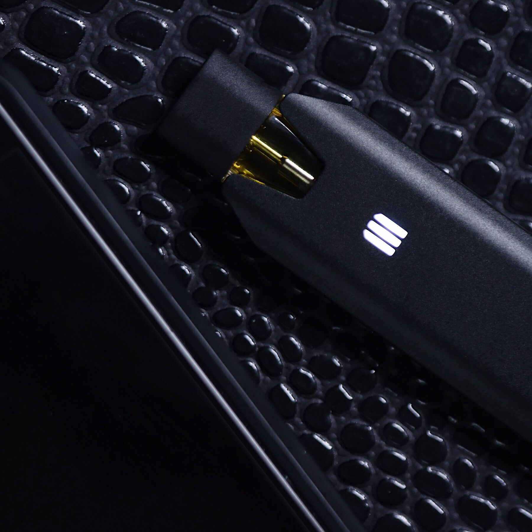 A big black weed pen battery with its weed vape pod attaches sits on a metal surface.