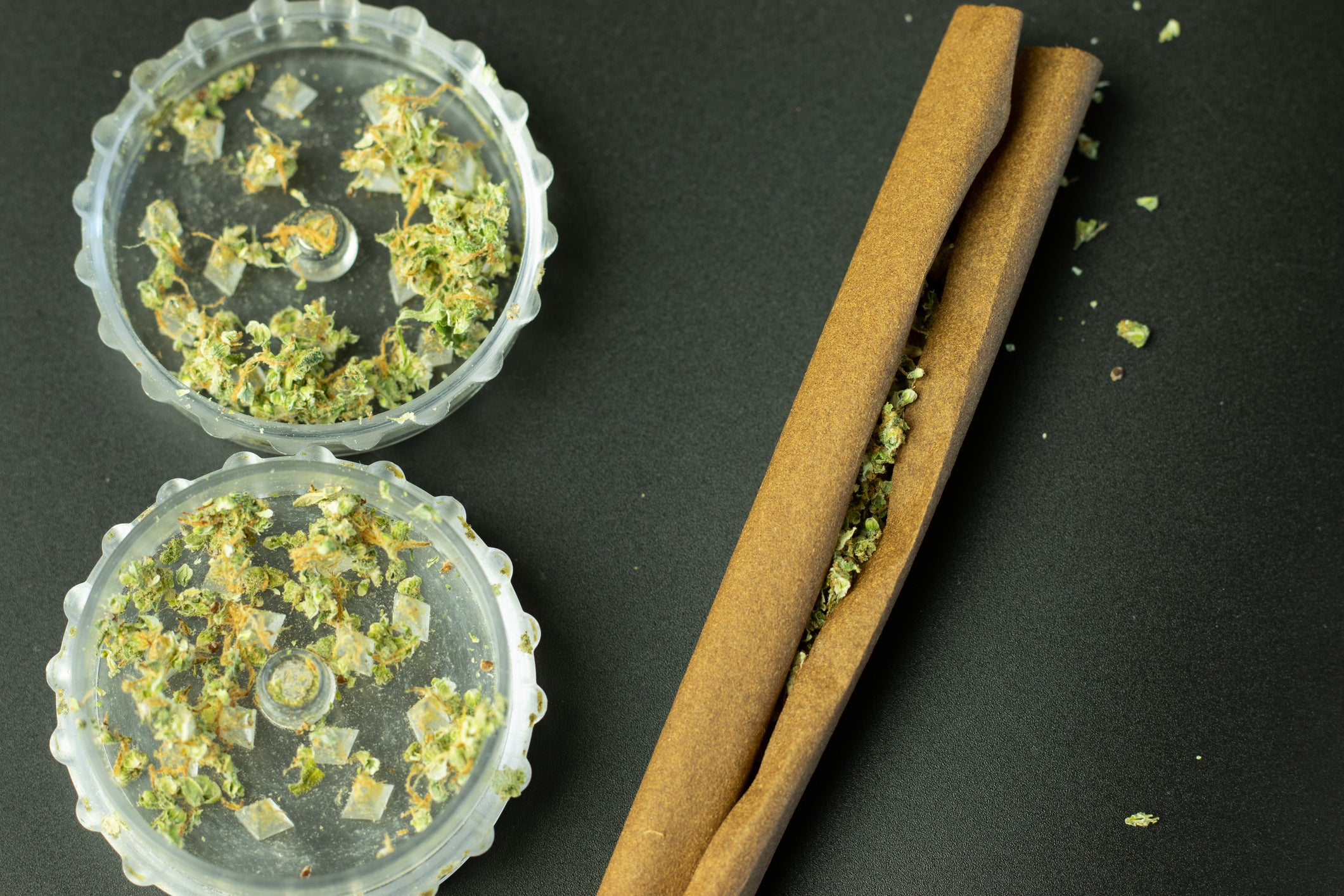 A blunt being rolled with cannabis flower lies next to the grinder.